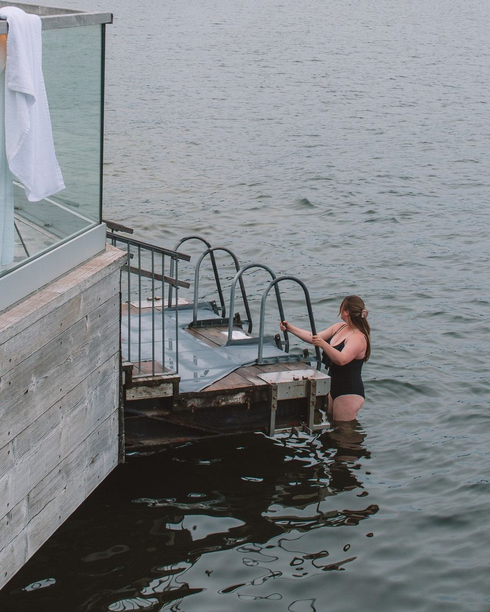 Woman climbing down a ladder into the sea from a sauna deck