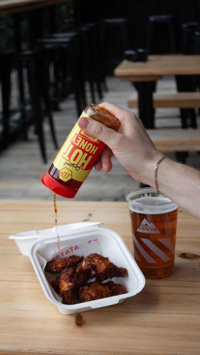 JD's hot honey bottle poured over wings next to a pint of beer