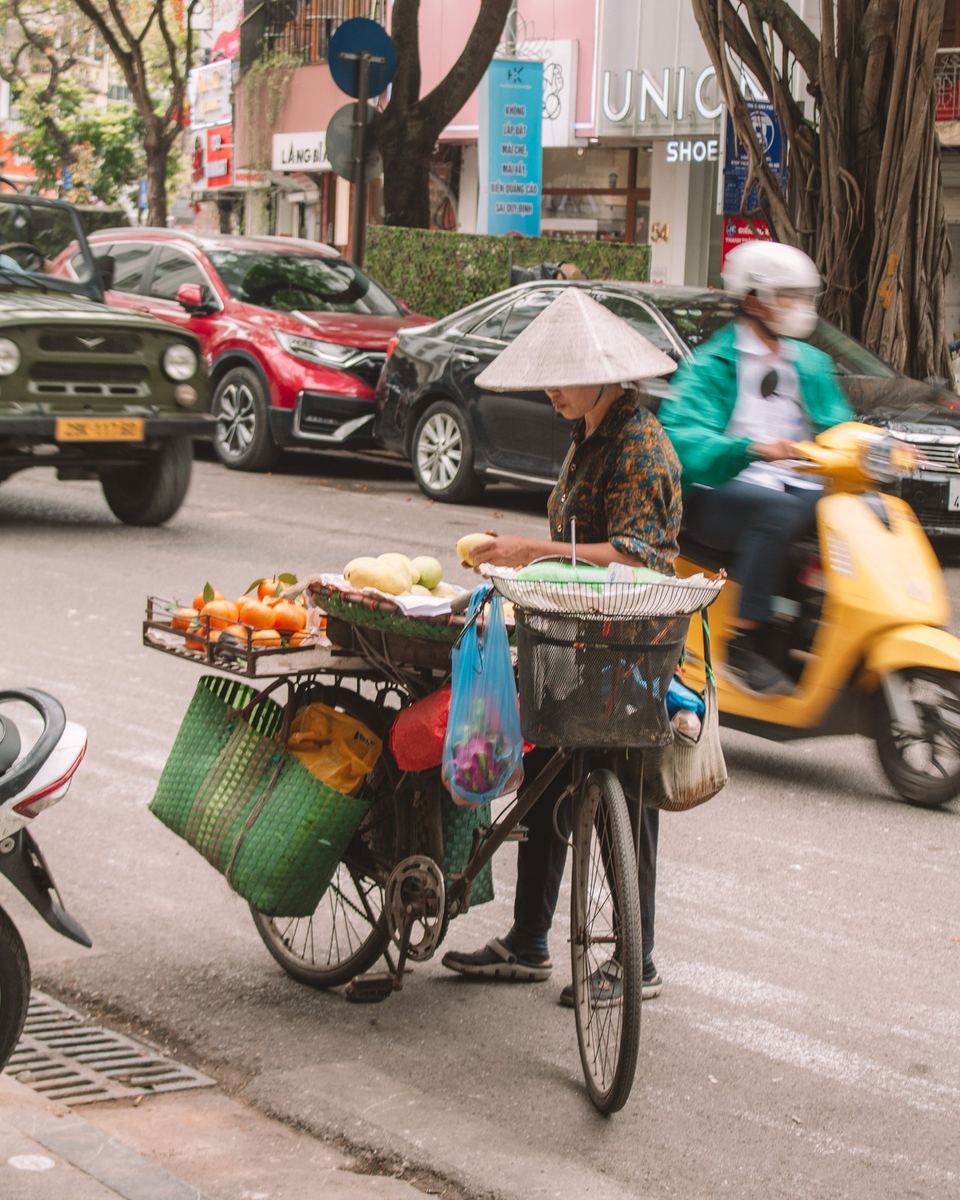 Street vendor pushing a bicycle laden with fruit through busy traffic